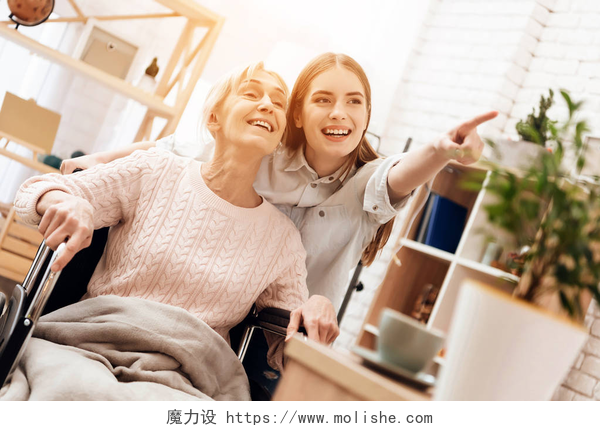 在卧室里的奶奶和孙女女孩护理老年妇女在家中, 骑在轮椅上她